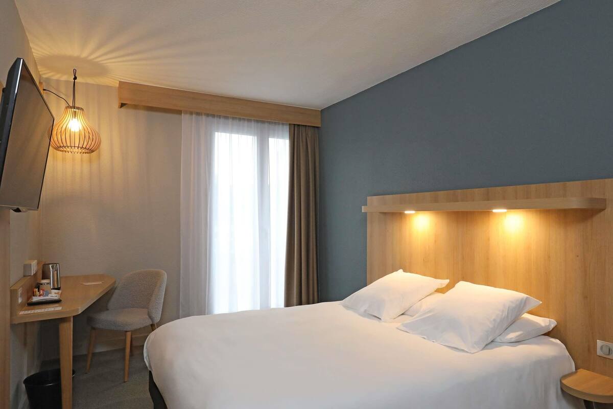 Une chambre d’hôtel équipée d’un lit, d’un bureau, d’une chaise, d’une télévision et d’une fenêtre avec des rideaux.