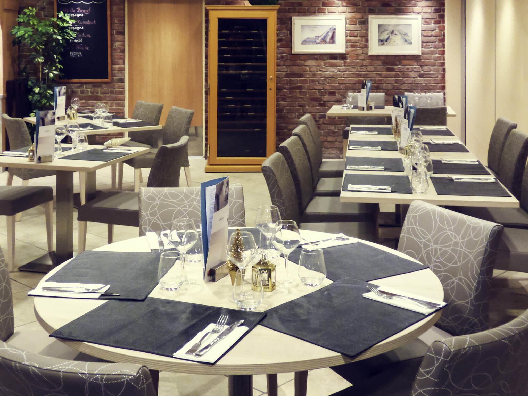 Un restaurant avec des tables rondes, des chaises à revêtement gris et un mur en briques orné de tableaux.