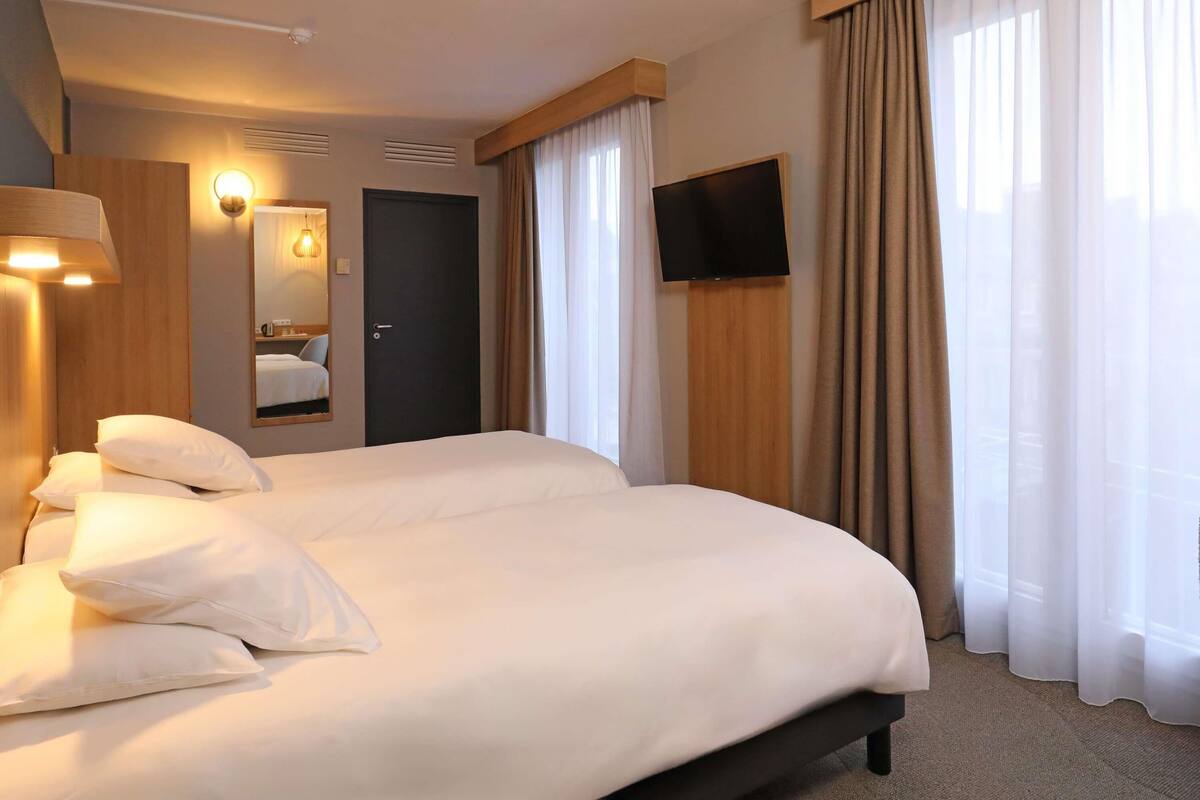 Une chambre d’hôtel avec deux lits, un téléviseur à écran plat, un miroir et une fenêtre avec des rideaux.