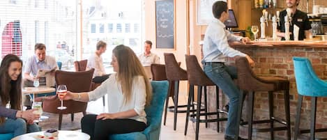A bar area with stools, a bartender, and a city view through large windows.