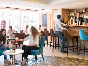 Un espace bar avec des tabourets, un barman et une vue sur la ville grâce à de grandes fenêtres.