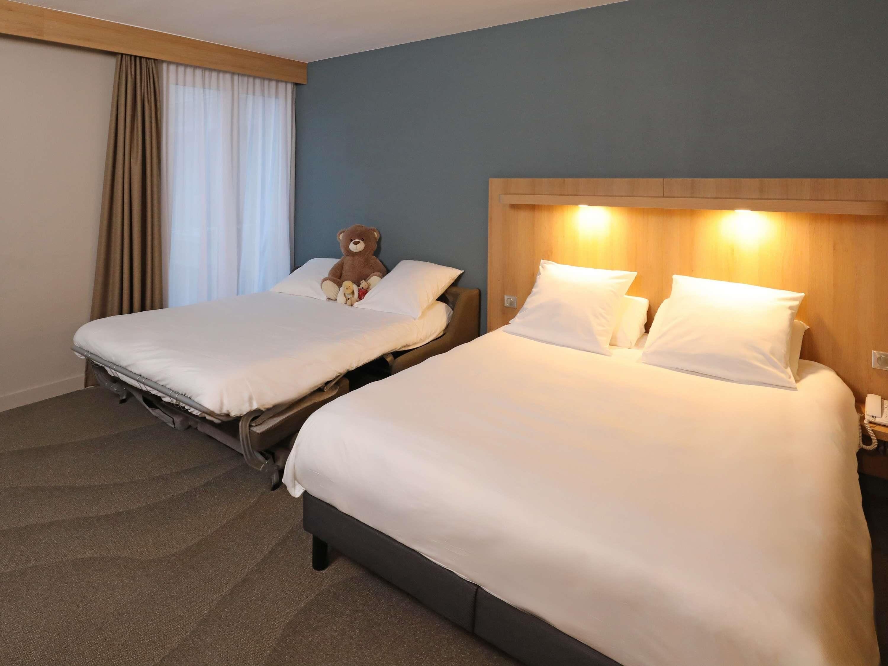 Two single beds with white linens, a wooden headboard, and a bedside table with a lamp.