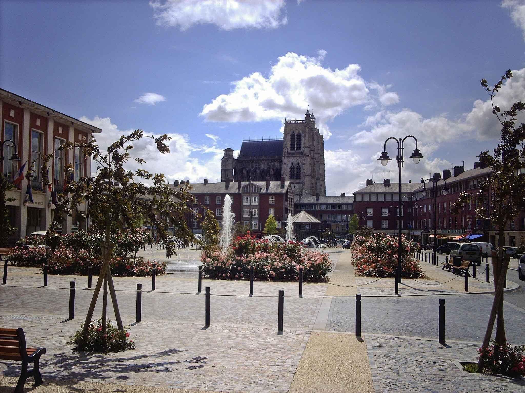 Una plaza pública con una fuente, bancos y un edificio histórico con una torre al fondo.