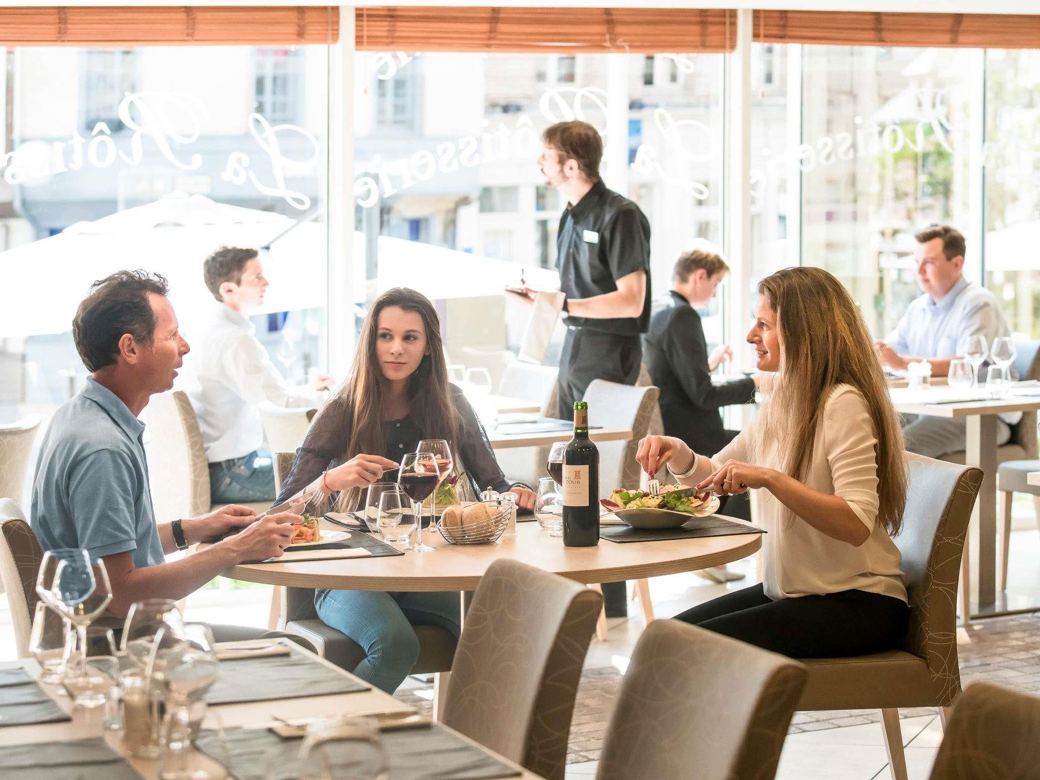 A group of people dining at an outdoor restaurant with large windows and a casual setting.