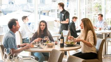 A group of people dining at an outdoor restaurant with large windows and a casual setting.