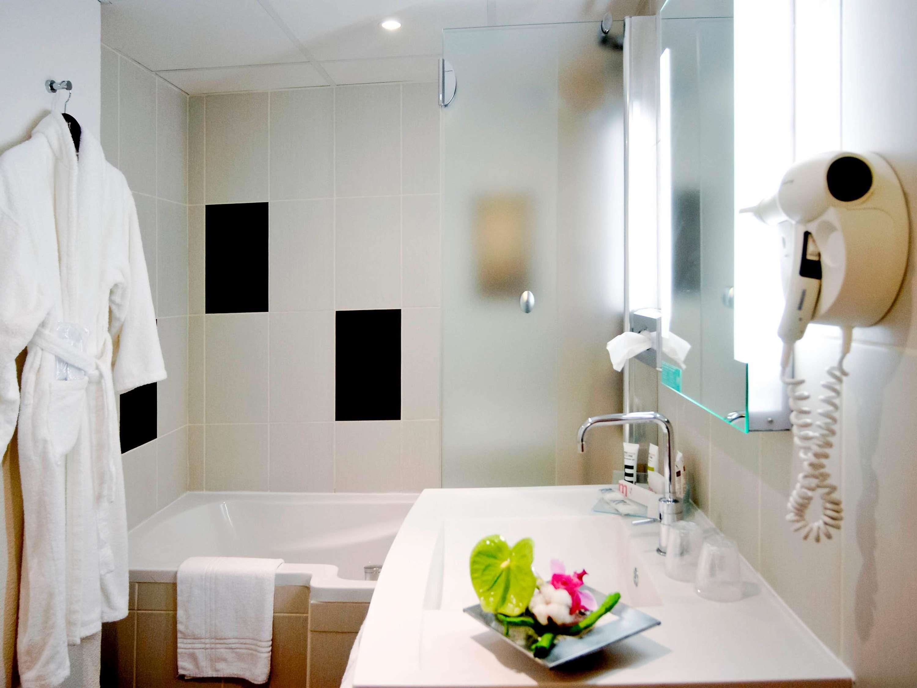 Une salle de bain moderne avec une baignoire, un lavabo avec un miroir et un sèche-cheveux fixé au mur.