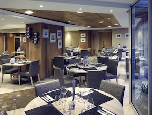 A modern restaurant with round tables, grey upholstered chairs, and a wooden accent wall.