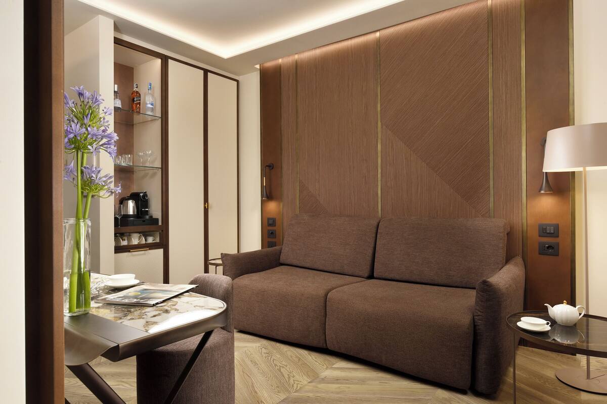 Een moderne woonkamer met een bruine bank, een glazen salontafel en een vaas met bloemen.