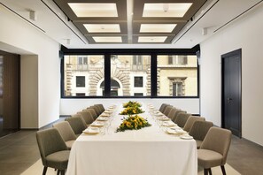 Een vergaderzaal met een lange tafel, stoelen en een uitzicht op gebouwen door grote ramen.