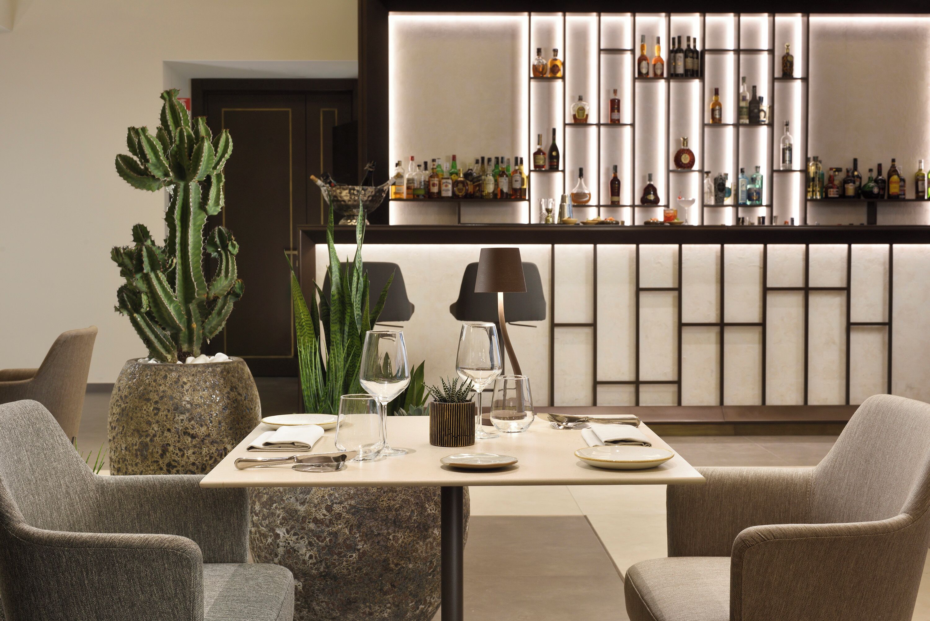 A bar area with shelves of bottles, a cactus plant, and a table set for dining.