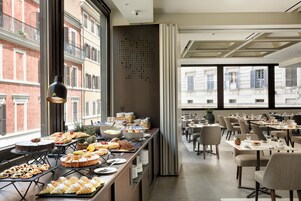 A hotel dining area with buffet-style food, tables, chairs, and large windows with a city view.