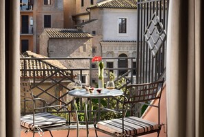 A balcony with two striped chairs, a small round table, and a vase with a red flower.