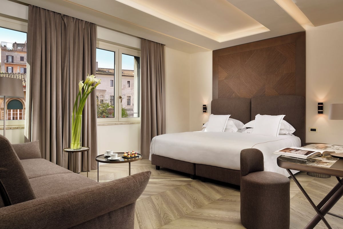 Een moderne hotelkamer met een groot bed, een sofa, een tafeltje en stadszicht door grote ramen.