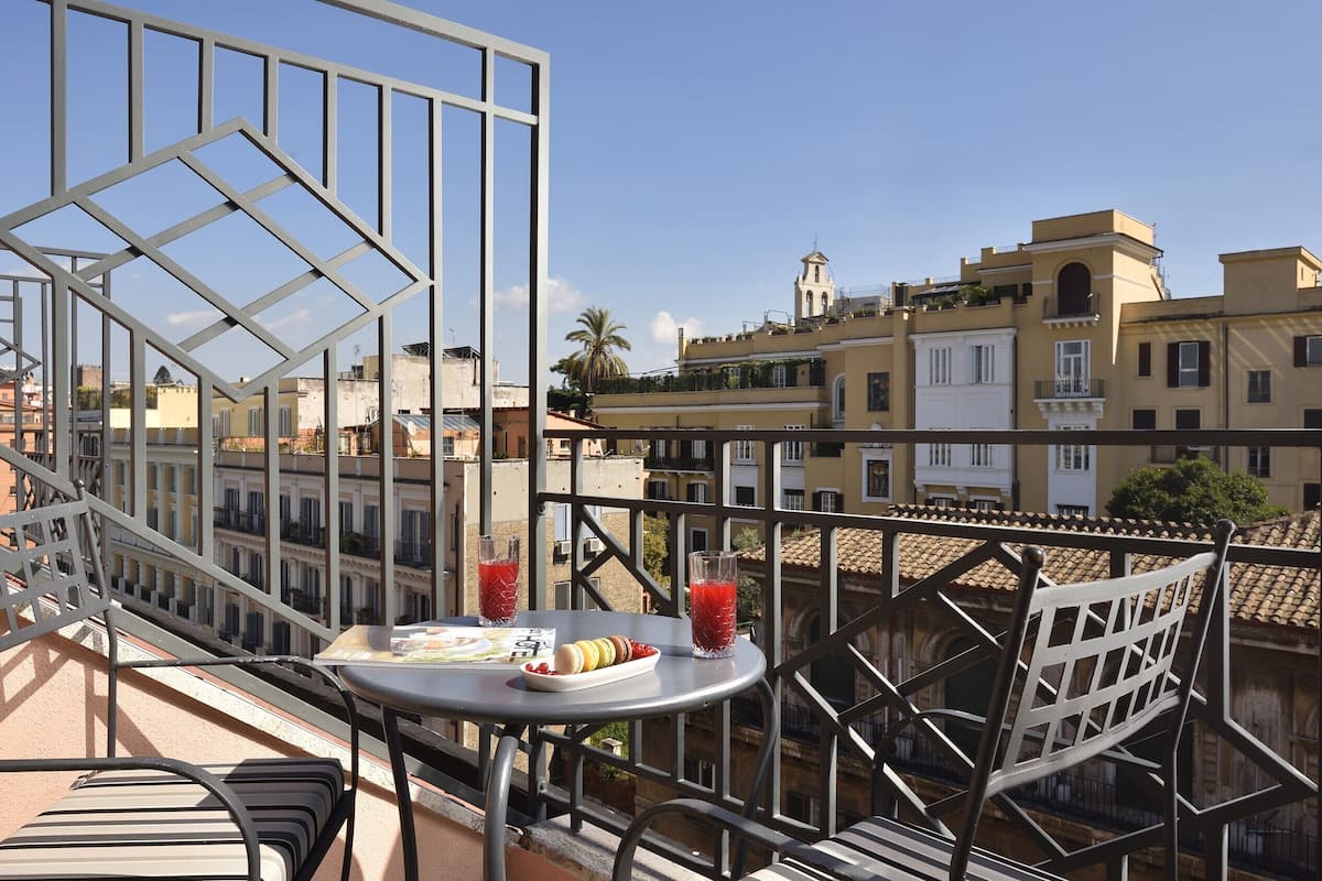 Een balkon met een tafel gedekt voor twee personen, compleet met een bord macarons en twee glazen rode drank.