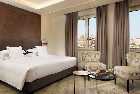A hotel room with a large bed, two armchairs, a small table with glasses, and a view of the city through large windows. - FH55 Grand Hotel Palatino (Rome)