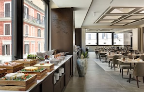 A modern dining area with a buffet setup, large windows, and a view of the cityscape.