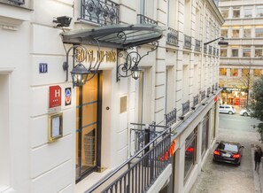 Fachada de un hotel con un cartel que dice "HOTEL DU BOIS", un hidrante visible y vista de la calle con coches aparcados.