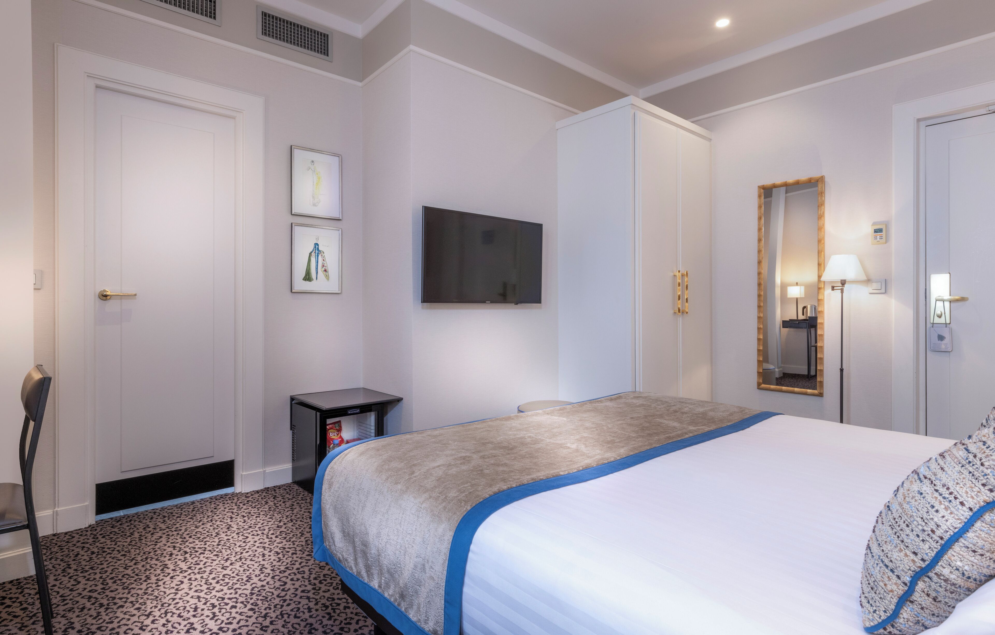 A hotel room with a bed, a television, a mirror, and a small table.