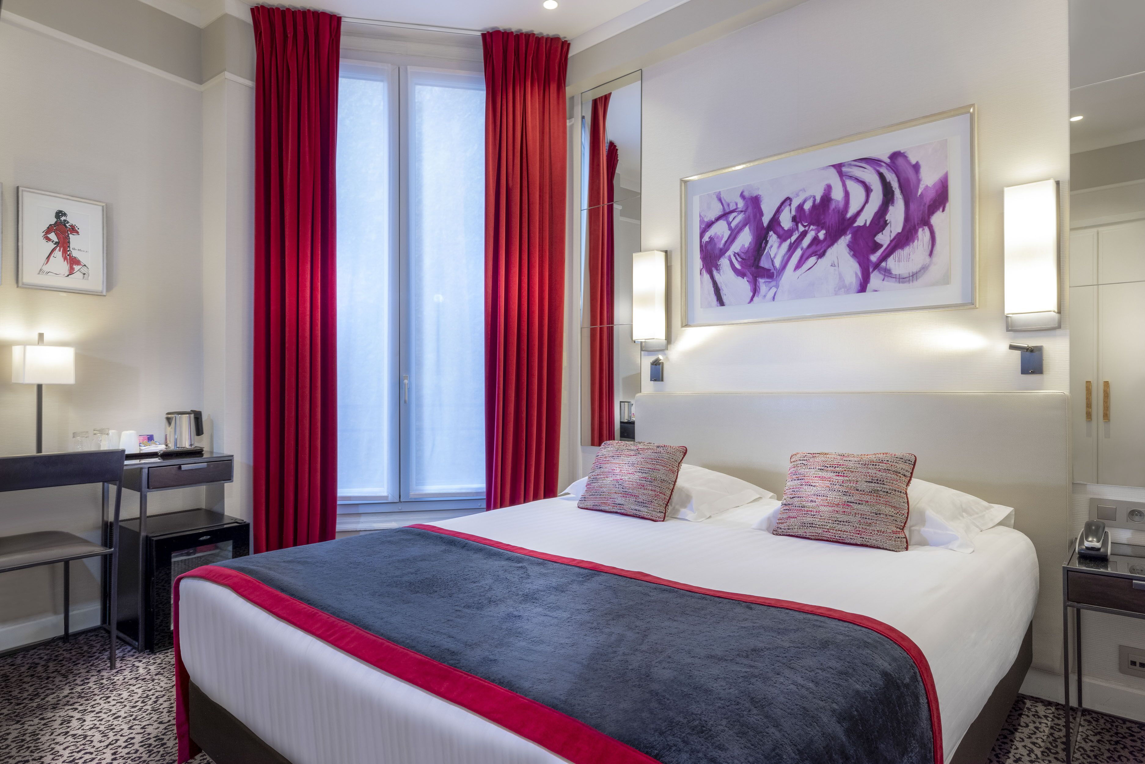 A hotel room with a large bed, red curtains, a desk, and a painting on the wall.