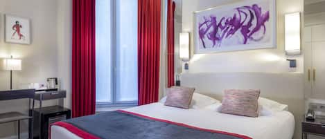 A hotel room with a large bed, red curtains, a desk, and a painting on the wall.