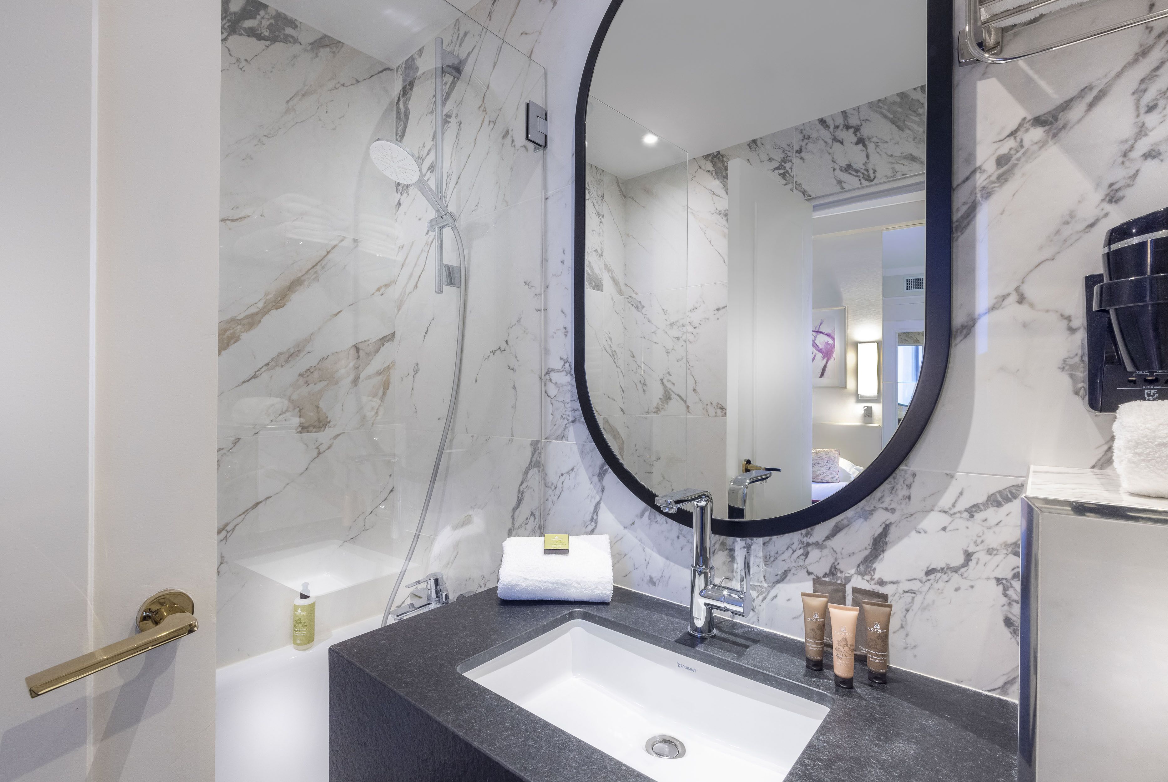 Un baño moderno con pared de mármol, un espejo grande, un lavamanos y artículos de aseo.