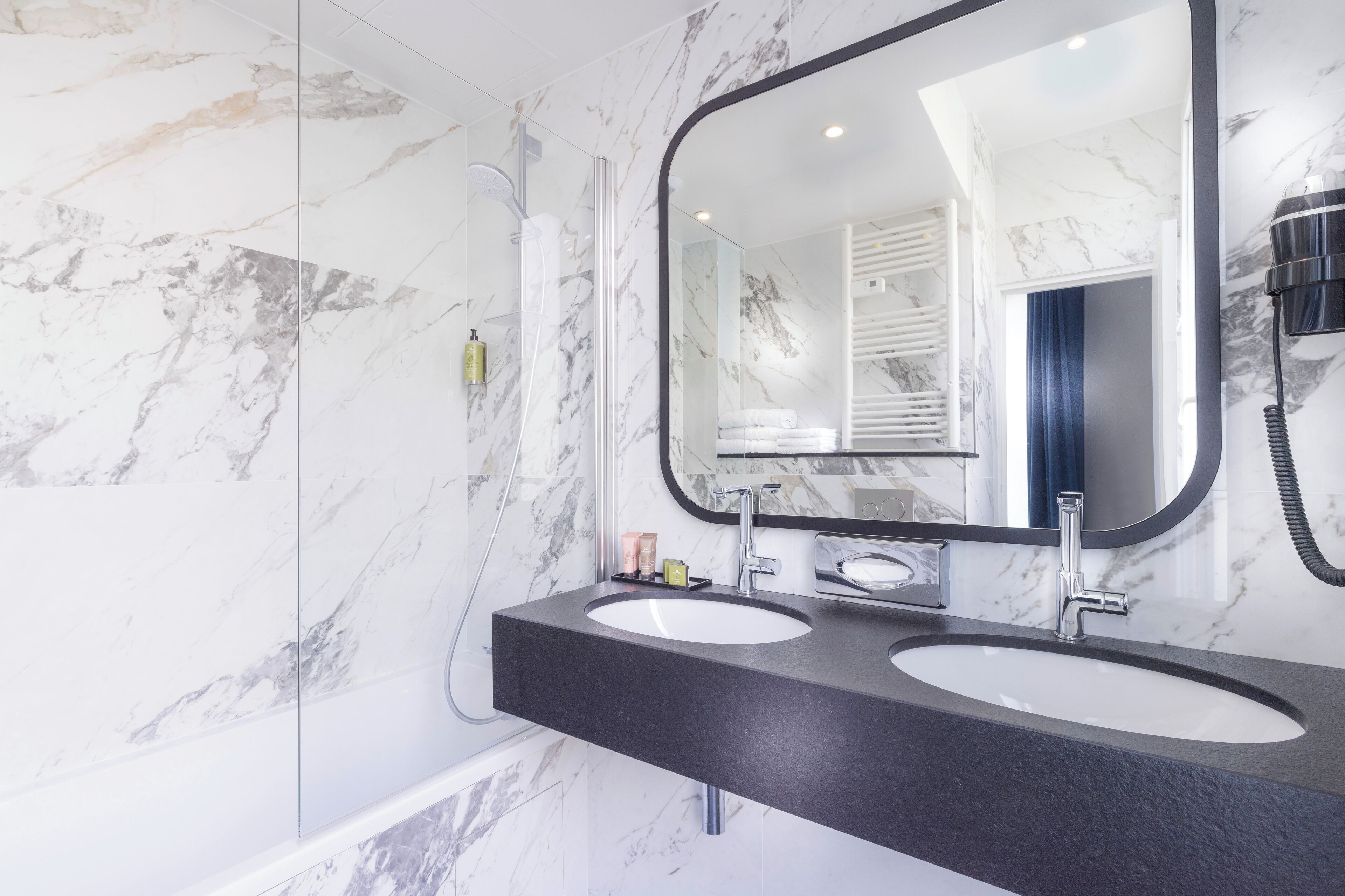 A bathroom with two sinks, a large mirror, and a hairdryer on the wall.