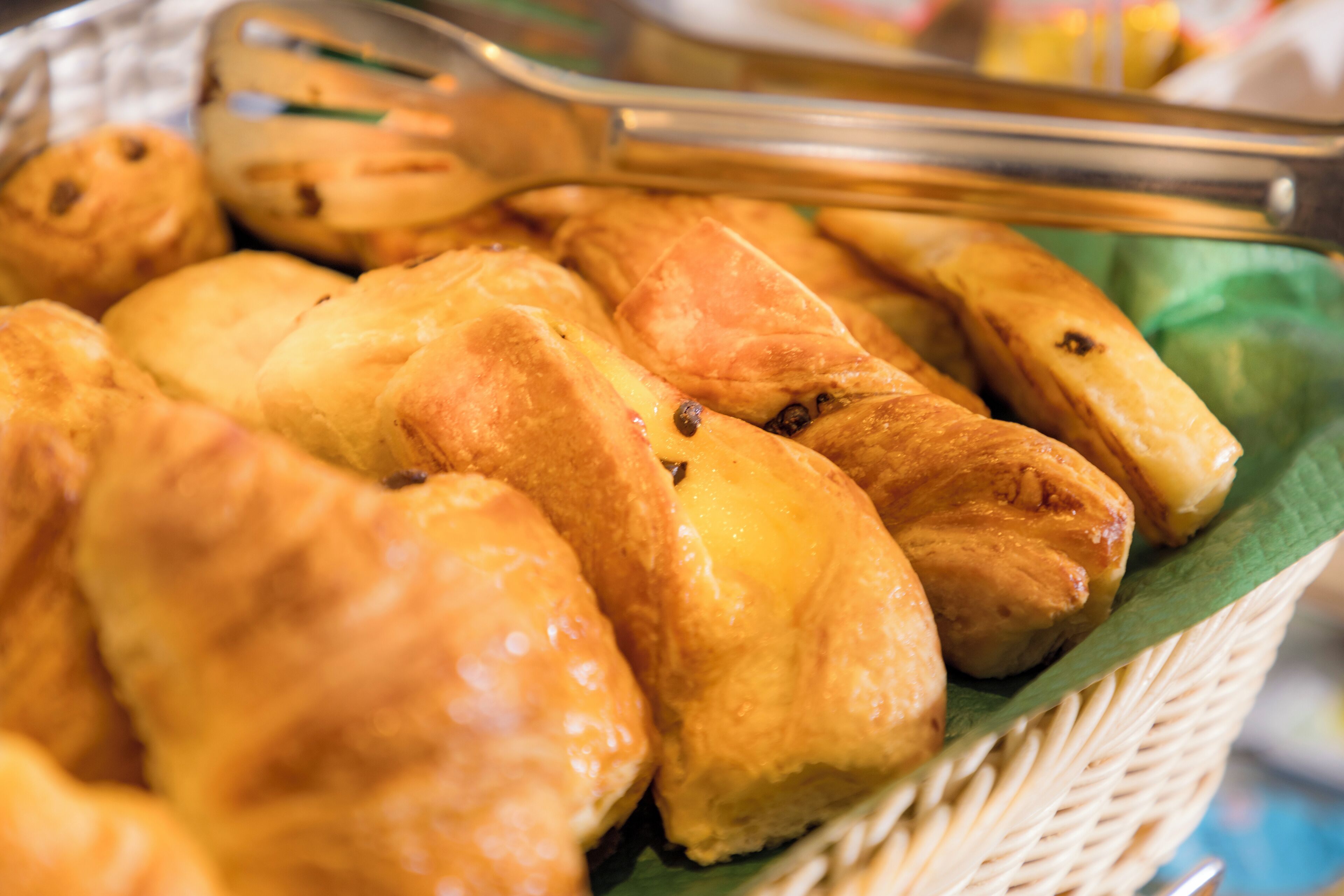 A basket of golden-brown pastries with a shiny glaze, placed on a green cloth.