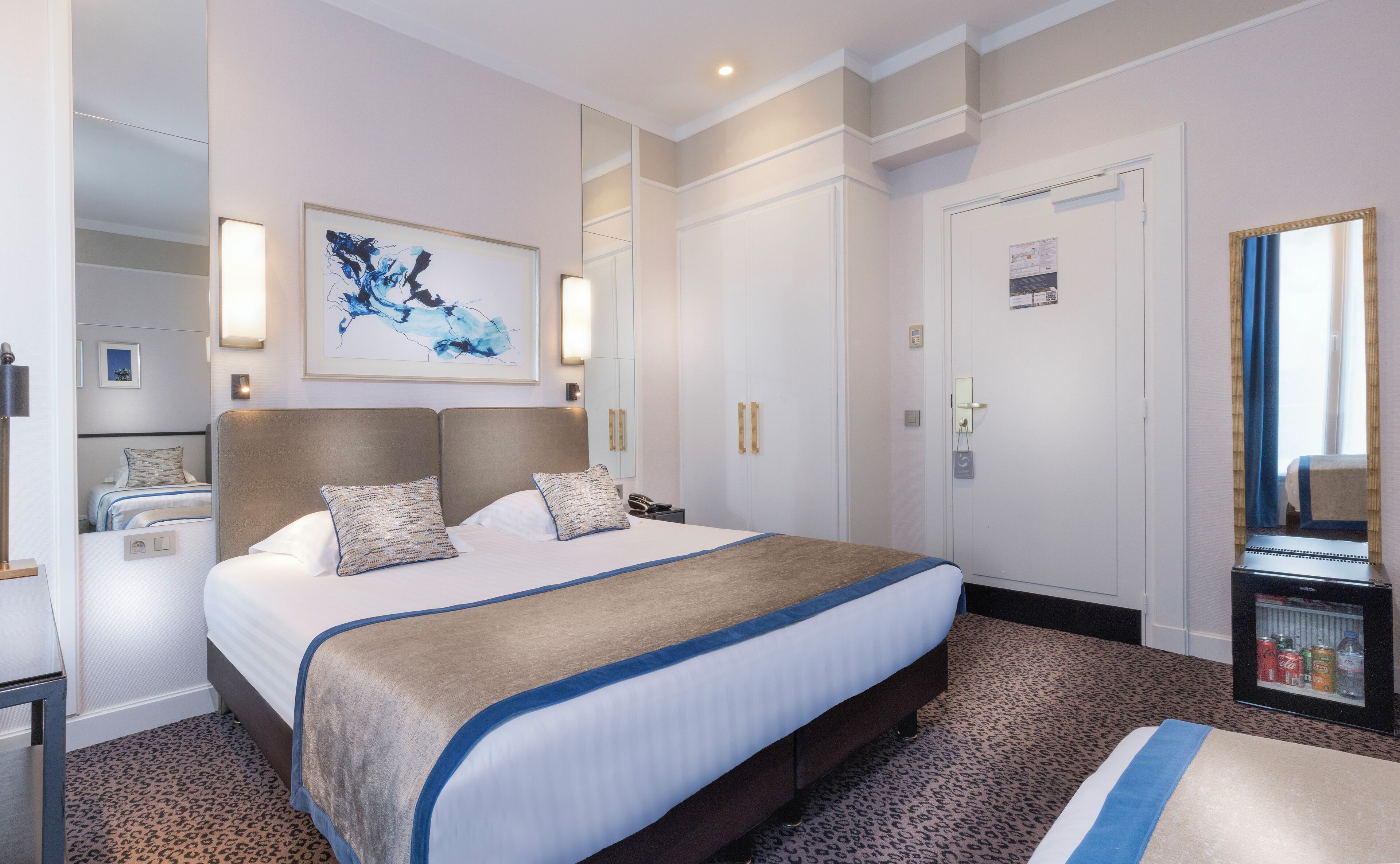 A hotel room with a large bed, a wardrobe, a desk, and a minibar.
