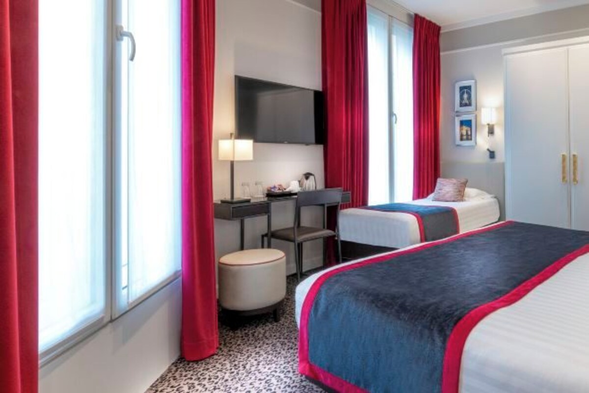 Una habitación de hotel con cama, escritorio, silla, una otomana redonda y armario.