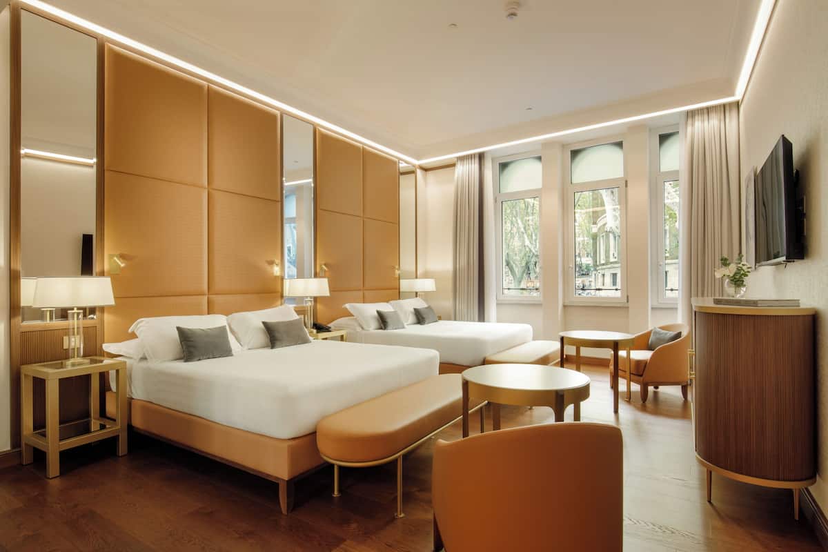 Camera d'albergo con un letto grande, due comodini con lampade, una zona salotto con una panca e sedie, un tavolino e una TV a parete.