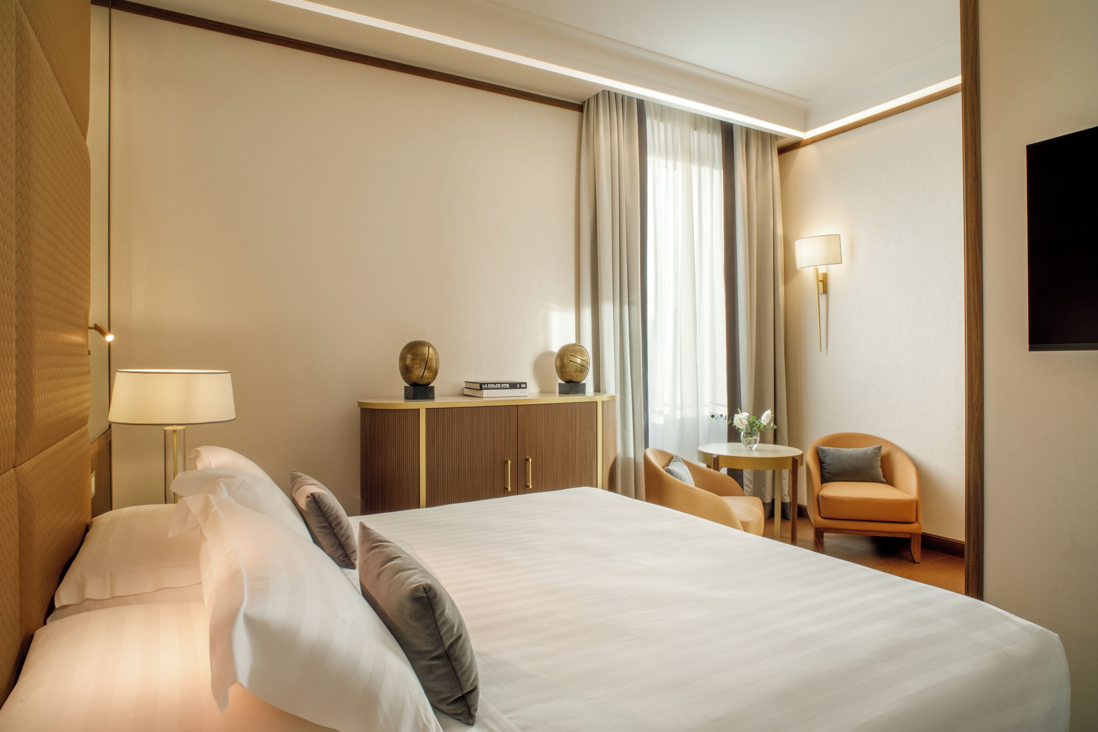 Una camera d'albergo con un letto grande, una scrivania con una lampada, una sedia e un televisore appeso al muro.