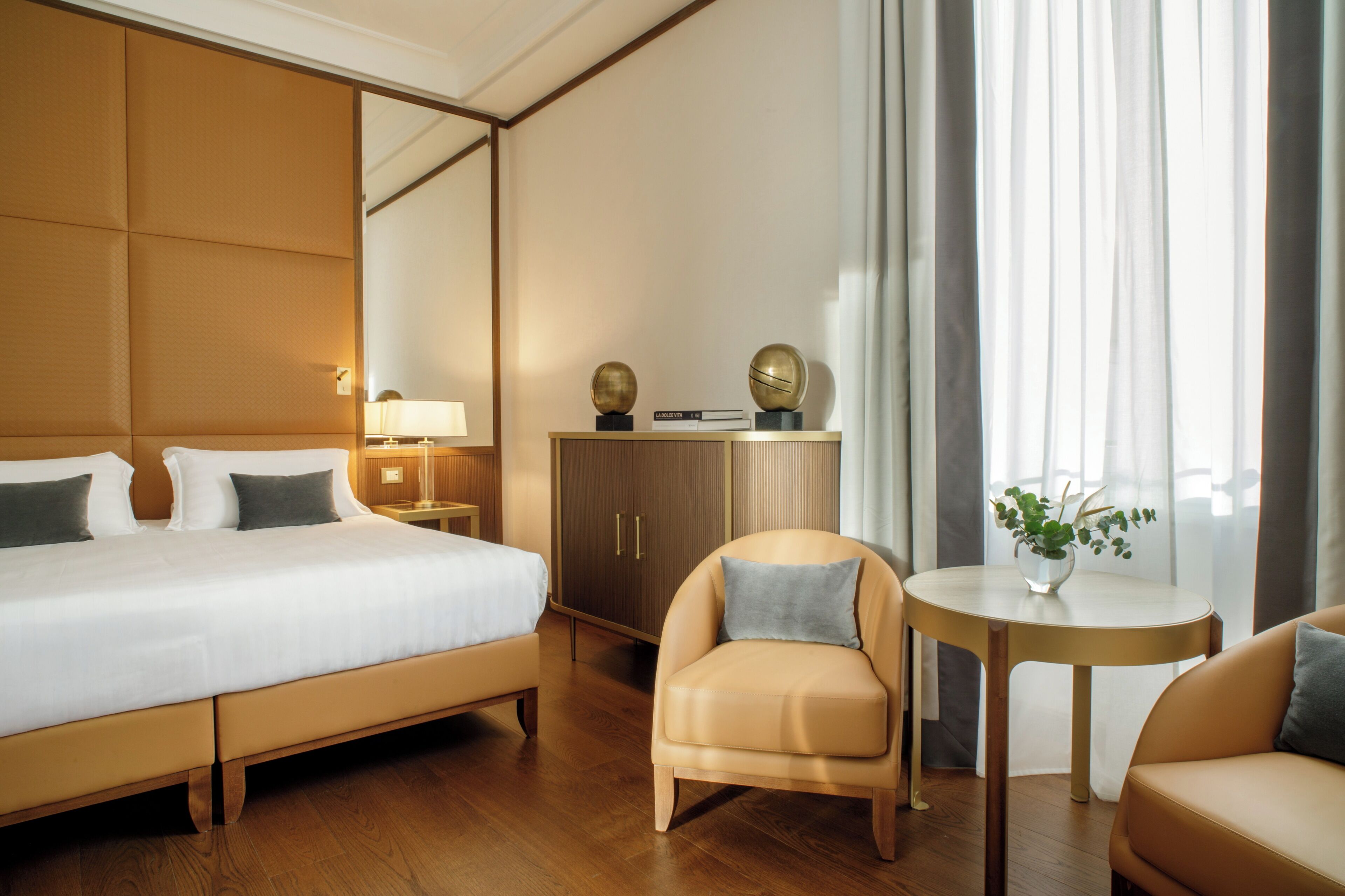 Una habitación de hotel con una cama grande, un armario de madera, una mesita redonda con una planta y un sofá.