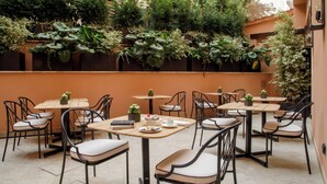 Un café al aire libre con varias mesas y sillas, rodeado de abundante vegetación y plantas.