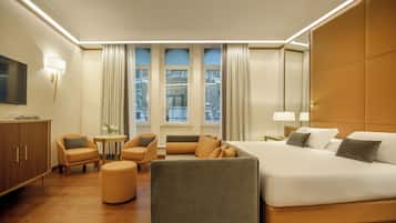 Quarto de hotel com uma cama grande, duas poltronas, uma mesa pequena e uma televisão.