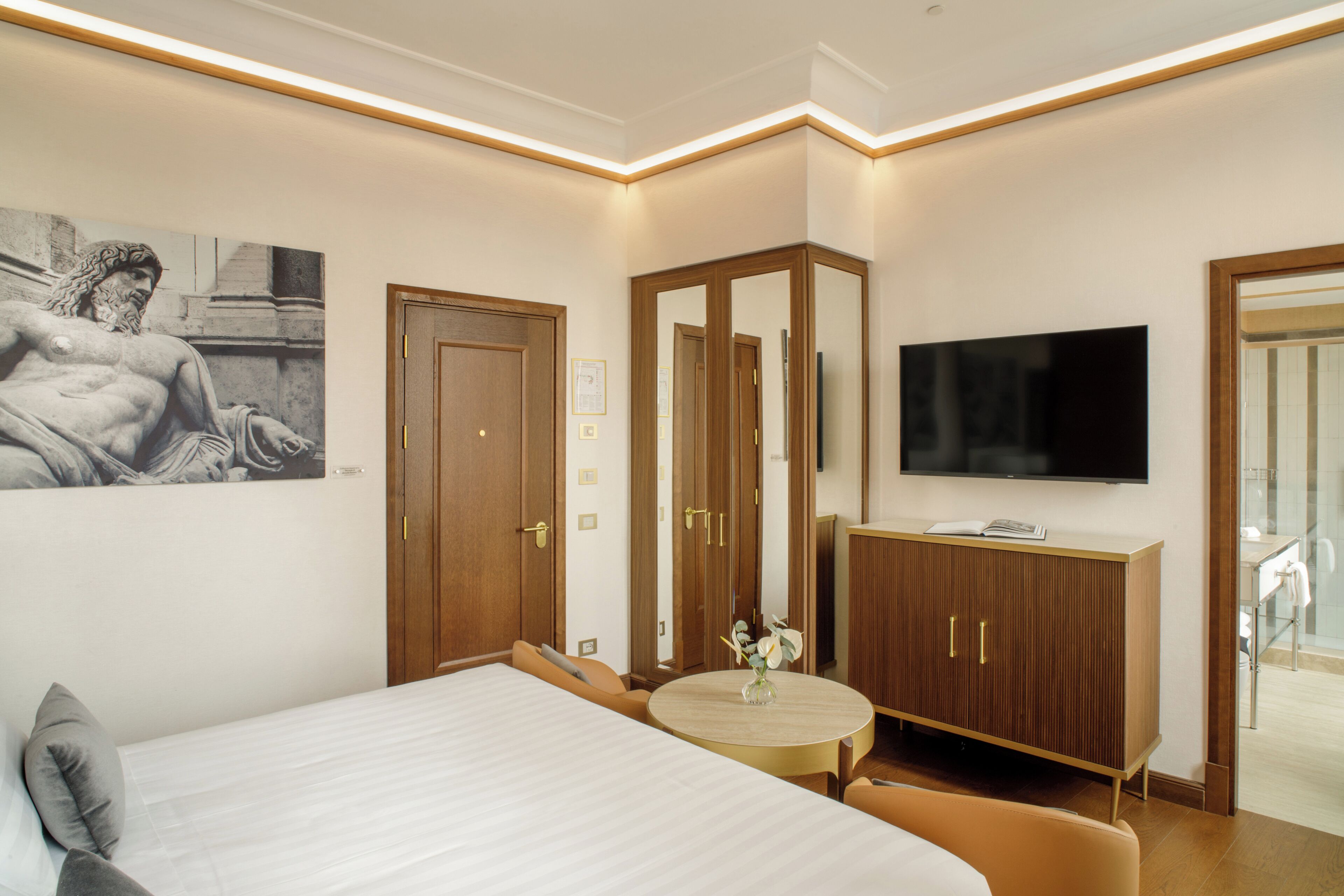 A hotel room with a bed, a TV, a wooden wardrobe, a round table, and a painting on the wall.