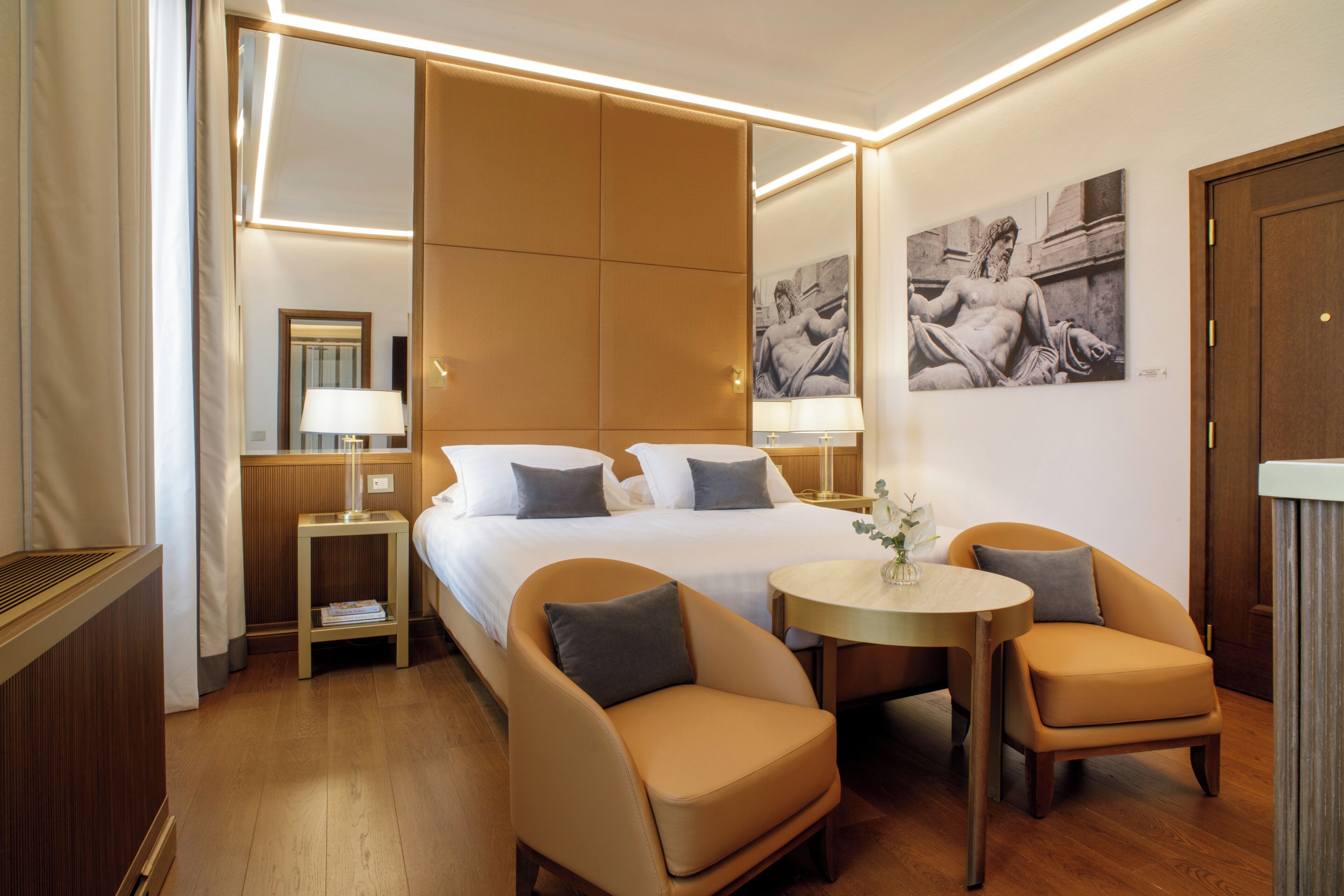 Camera d'albergo con un letto grande, due comodini, un tavolo rotondo con sedie e opere d'arte alle pareti.