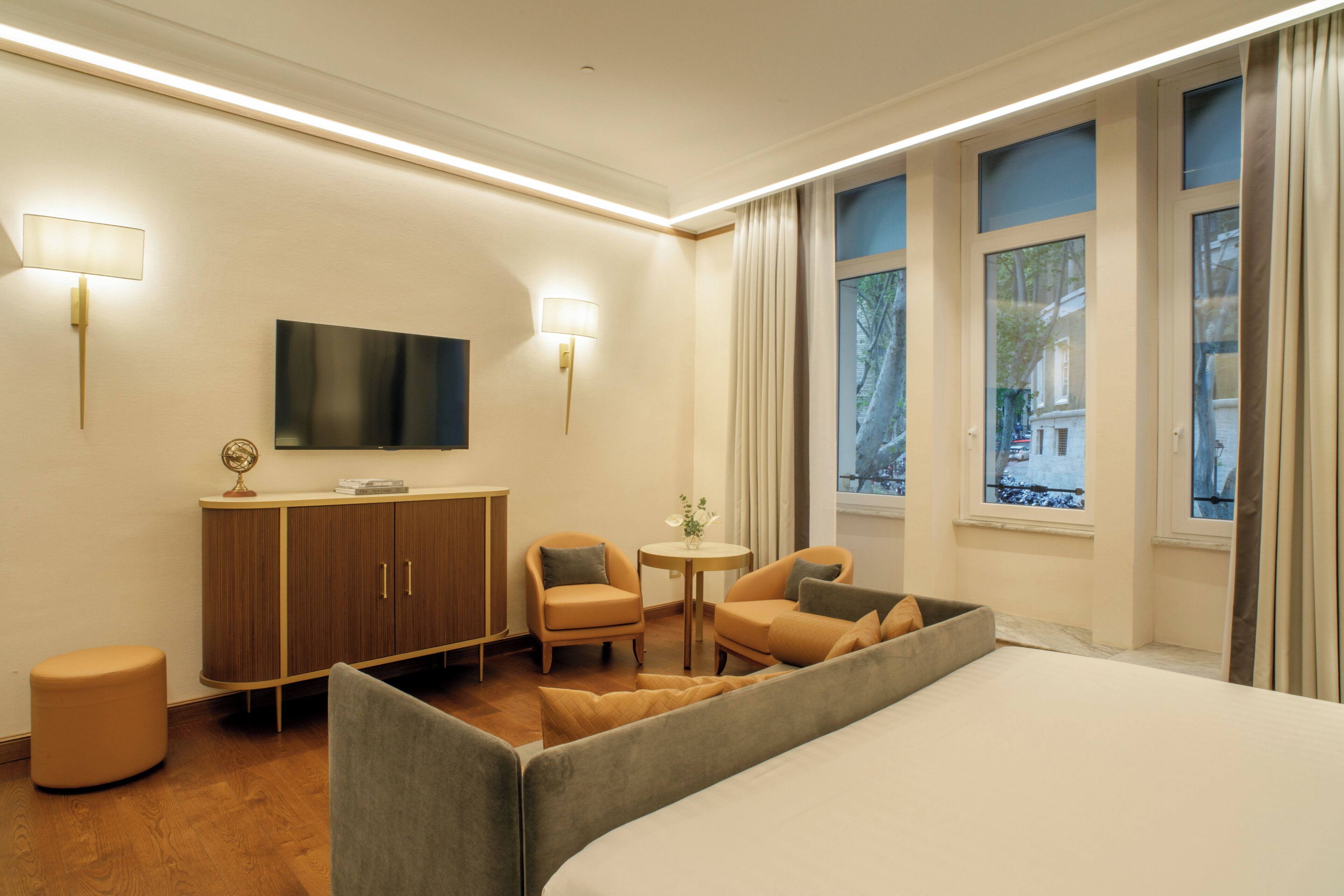 Habitación de hotel con cama, dos sillones, una mesita, un armario, televisor y ventanas con cortinas.