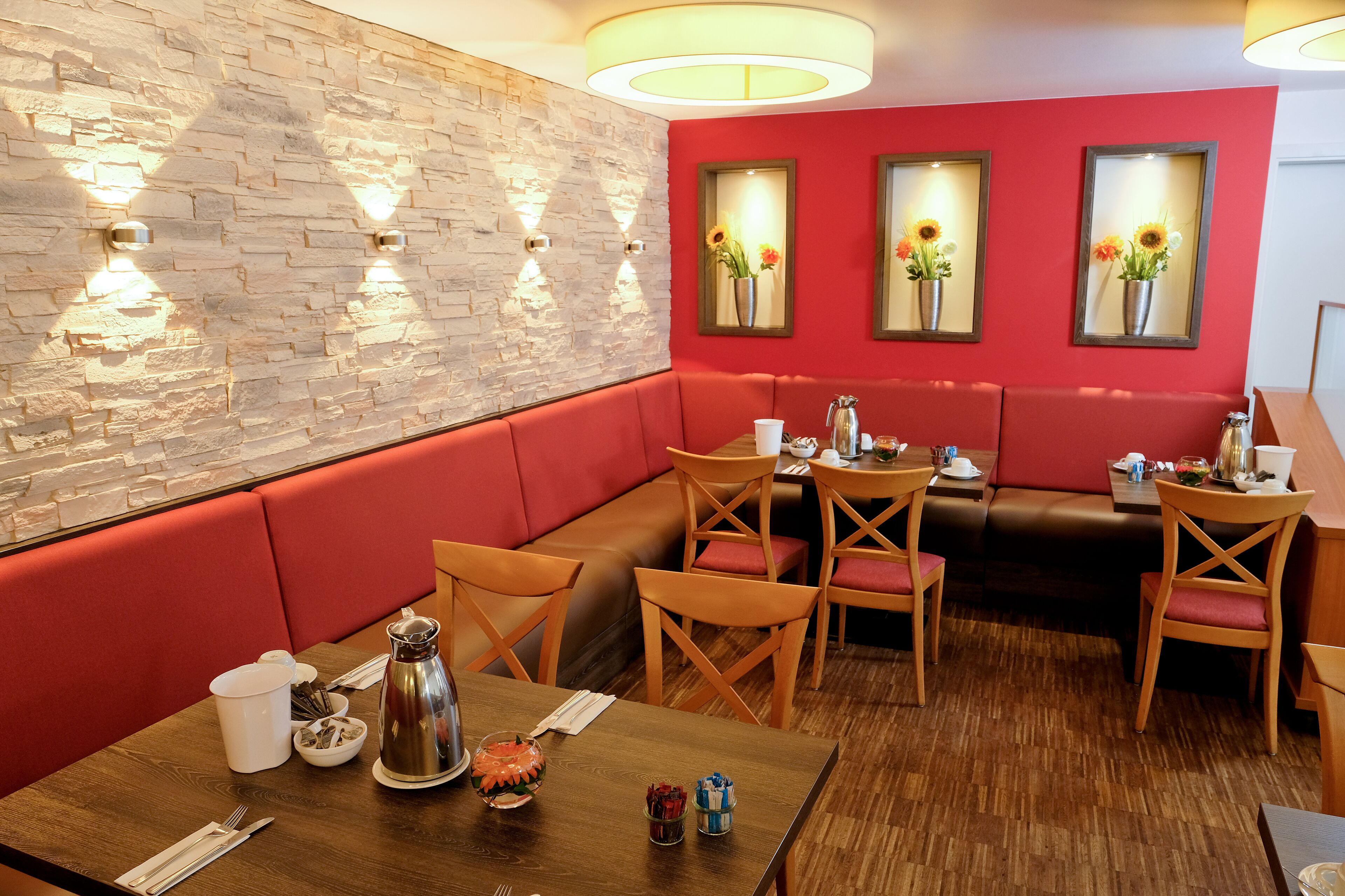 A restaurant with a stone wall, red seating, and framed sunflowers on the wall.