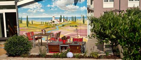 An outdoor seating area with a mural of a landscape, stone walls, and a table with chairs.