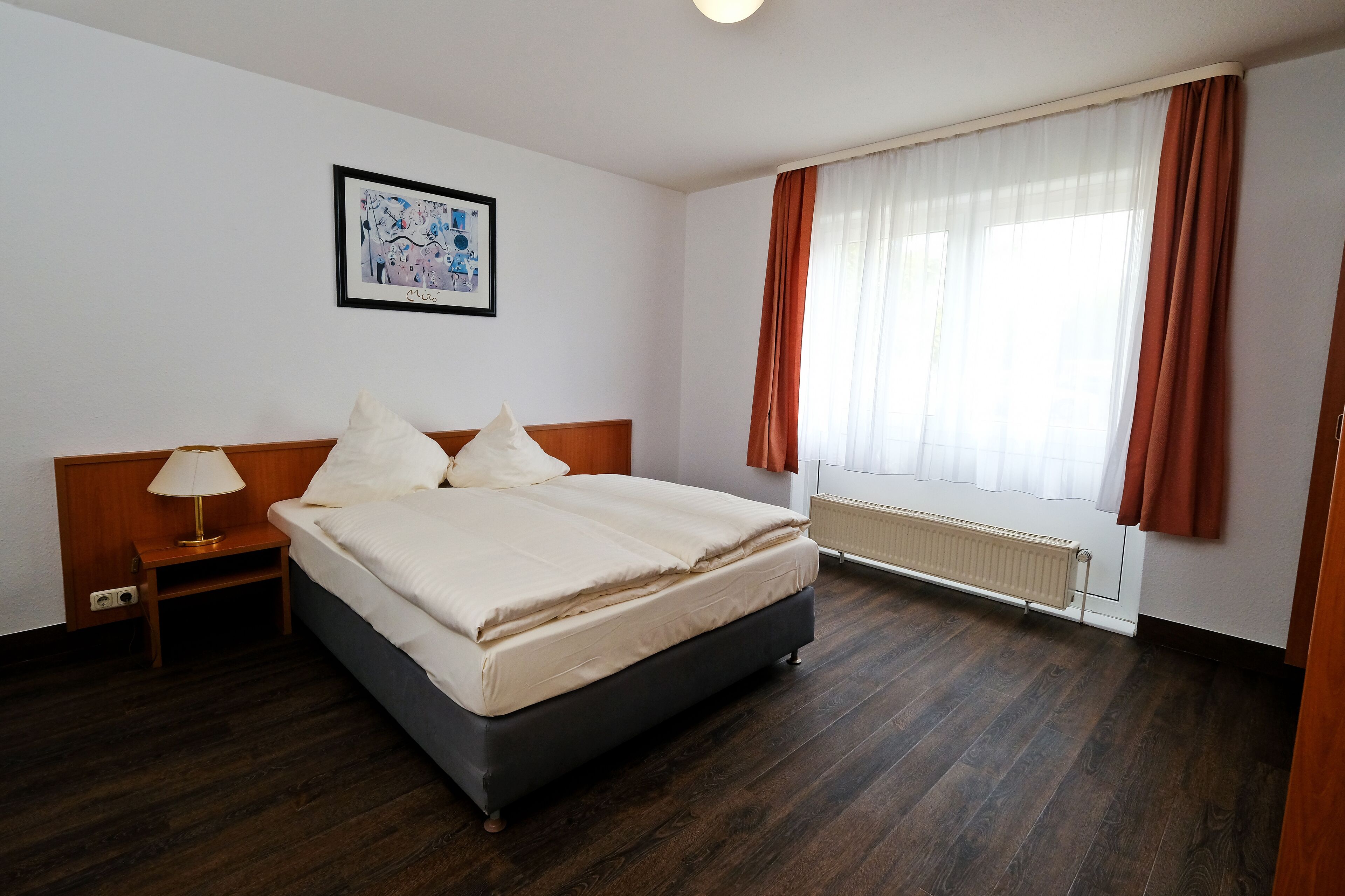 Habitación de hotel con una cama grande, una mesita de noche, una lámpara y una ventana con cortinas.