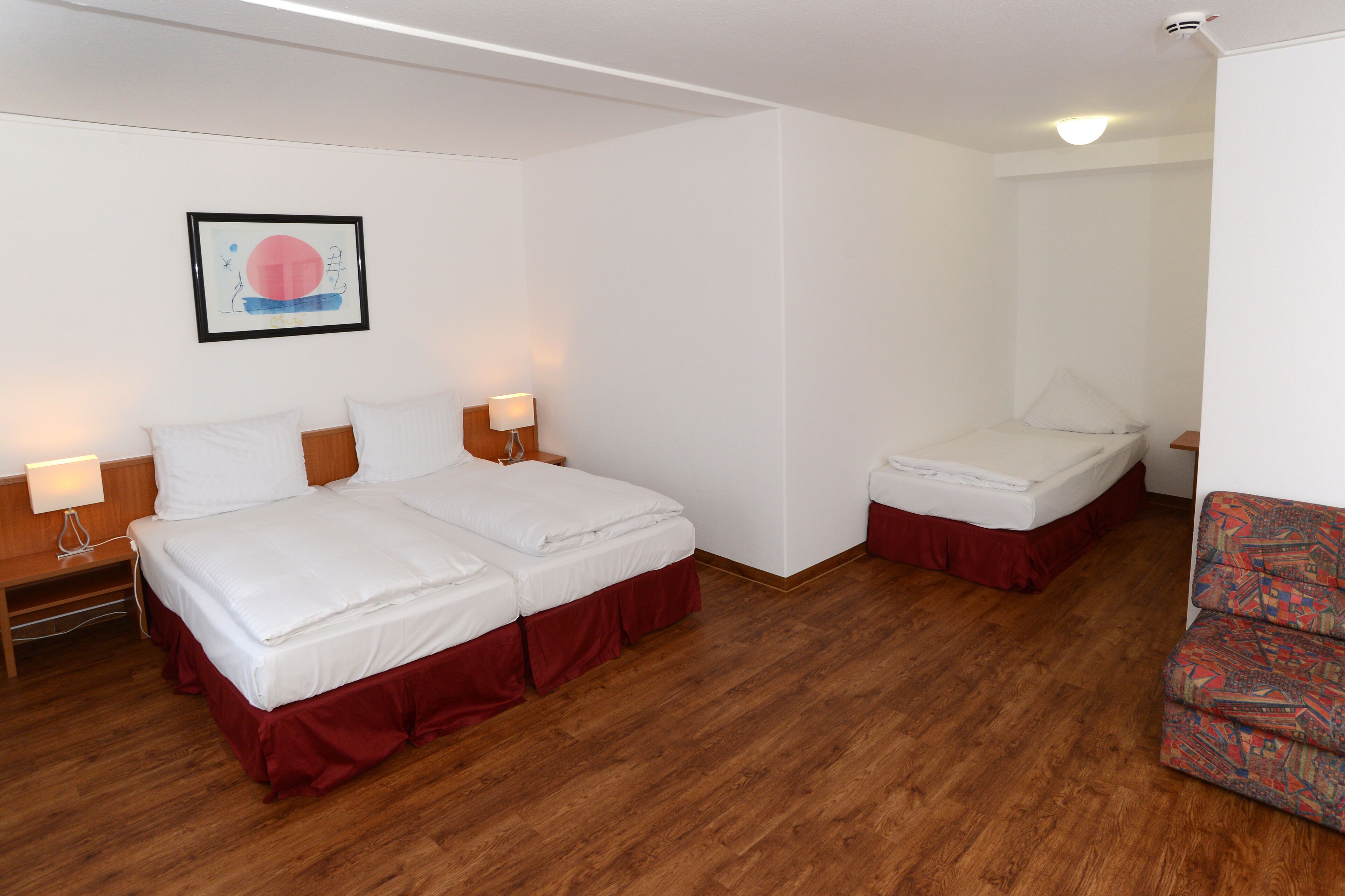 A hotel room with two beds, a small sofa, and a framed picture on the wall.