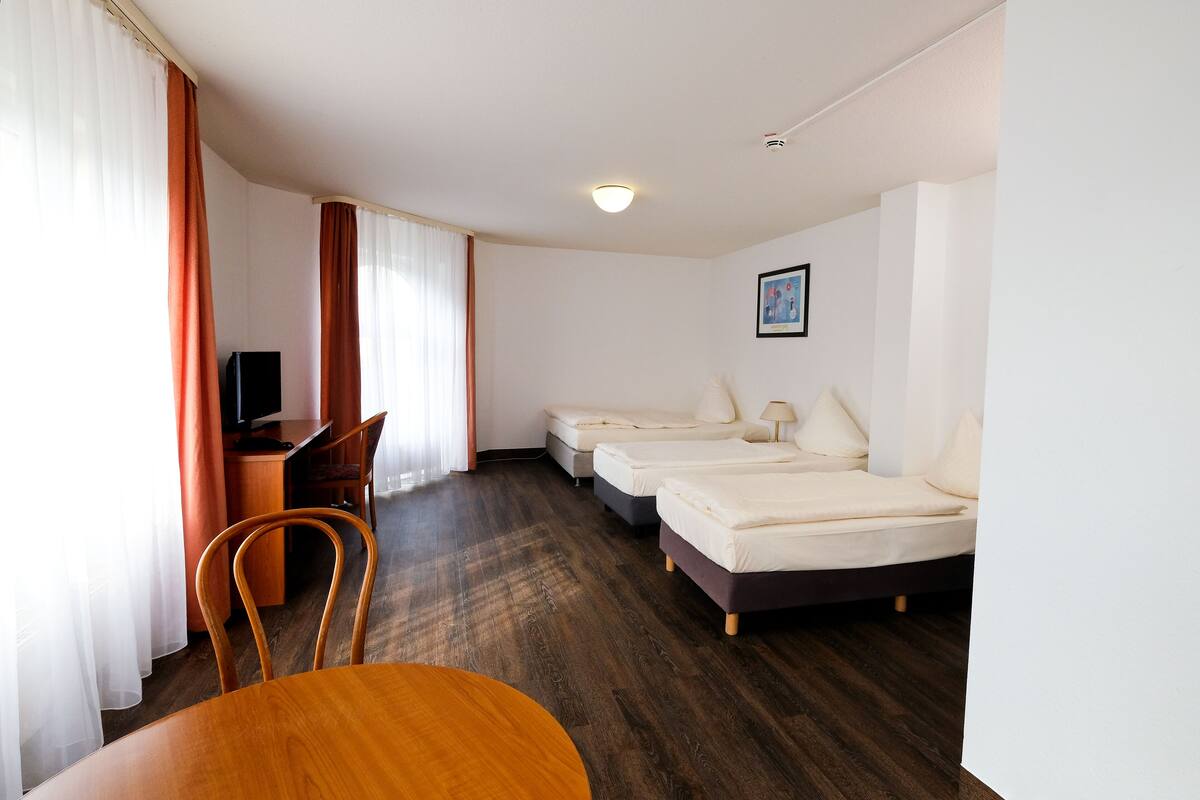 A hotel room with a wooden desk, a television, two beds, and a chair.