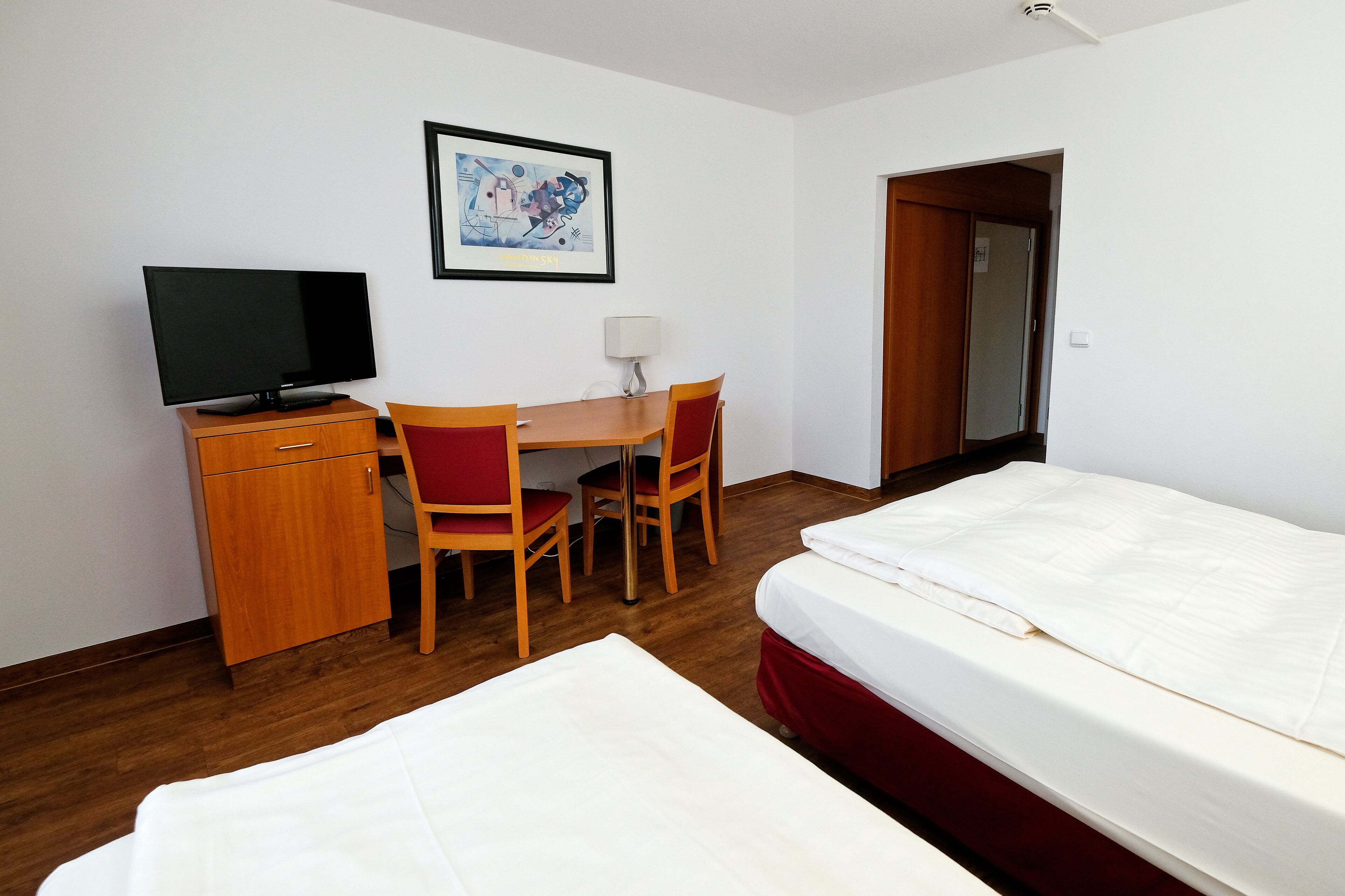 A hotel room with a bed, a desk with a chair, a television, and a framed picture on the wall.