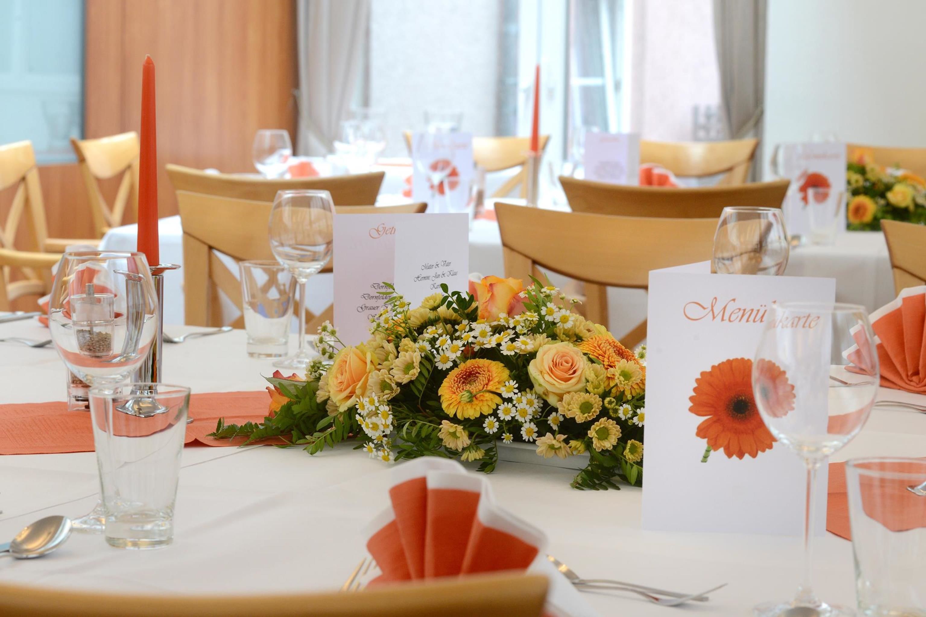 Une table à manger dressée avec de la verrerie, un menu et un centre de table composé de fleurs.