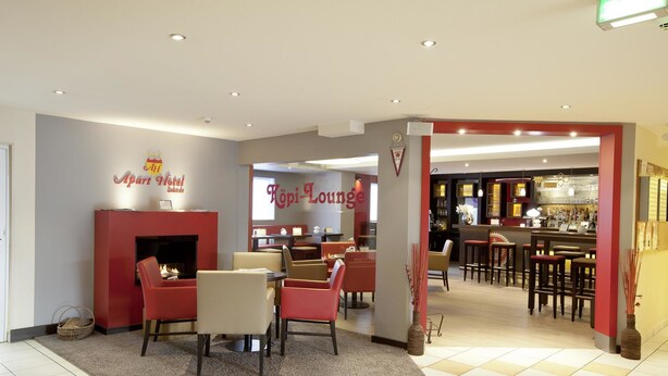 A hotel lobby with a fireplace, seating area, and a bar/lounge area. - Apart-Hotel Sehnde (Sehnde)