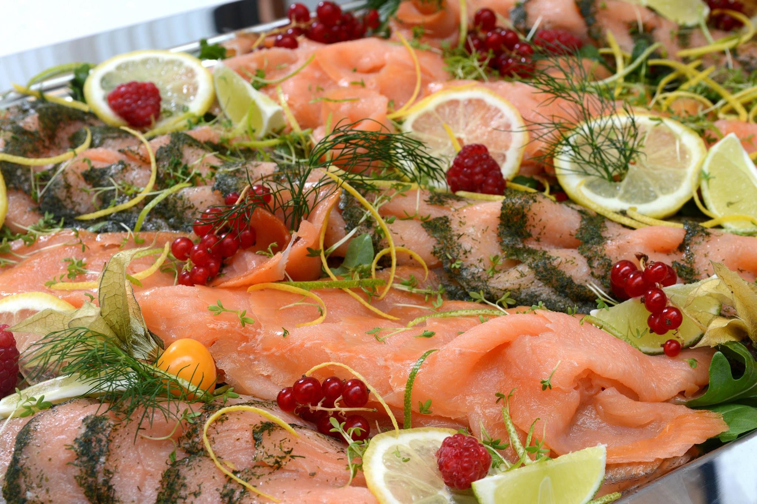 A platter of smoked salmon garnished with dill, lemon slices, and berries.