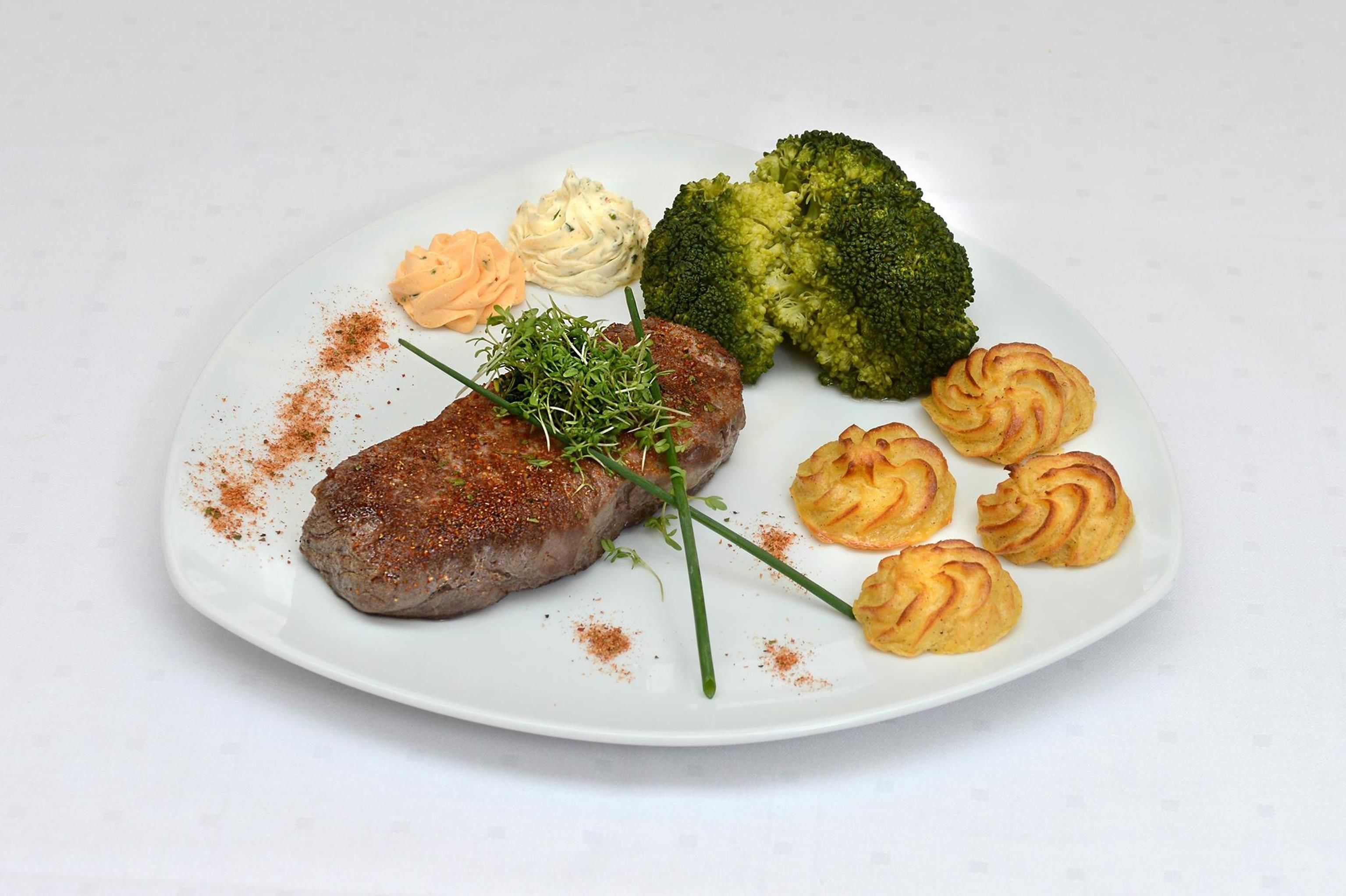 Un plato con una hamburguesa, brócoli y ñoquis de papa.