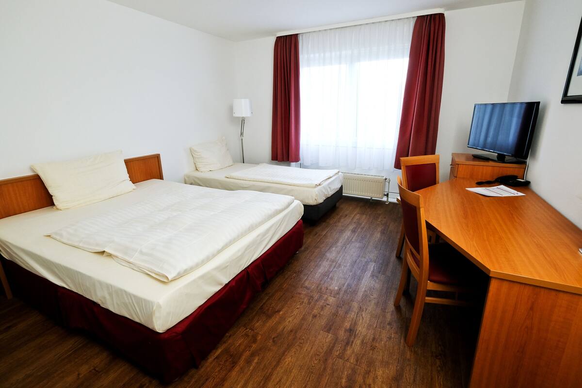 A hotel room with two beds, a desk, a chair, a television, and a window with curtains.