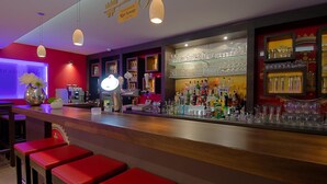 A bar area with red stools, a bar counter, and shelves with glasses and bottles. - Apart-Hotel Sehnde (Sehnde)