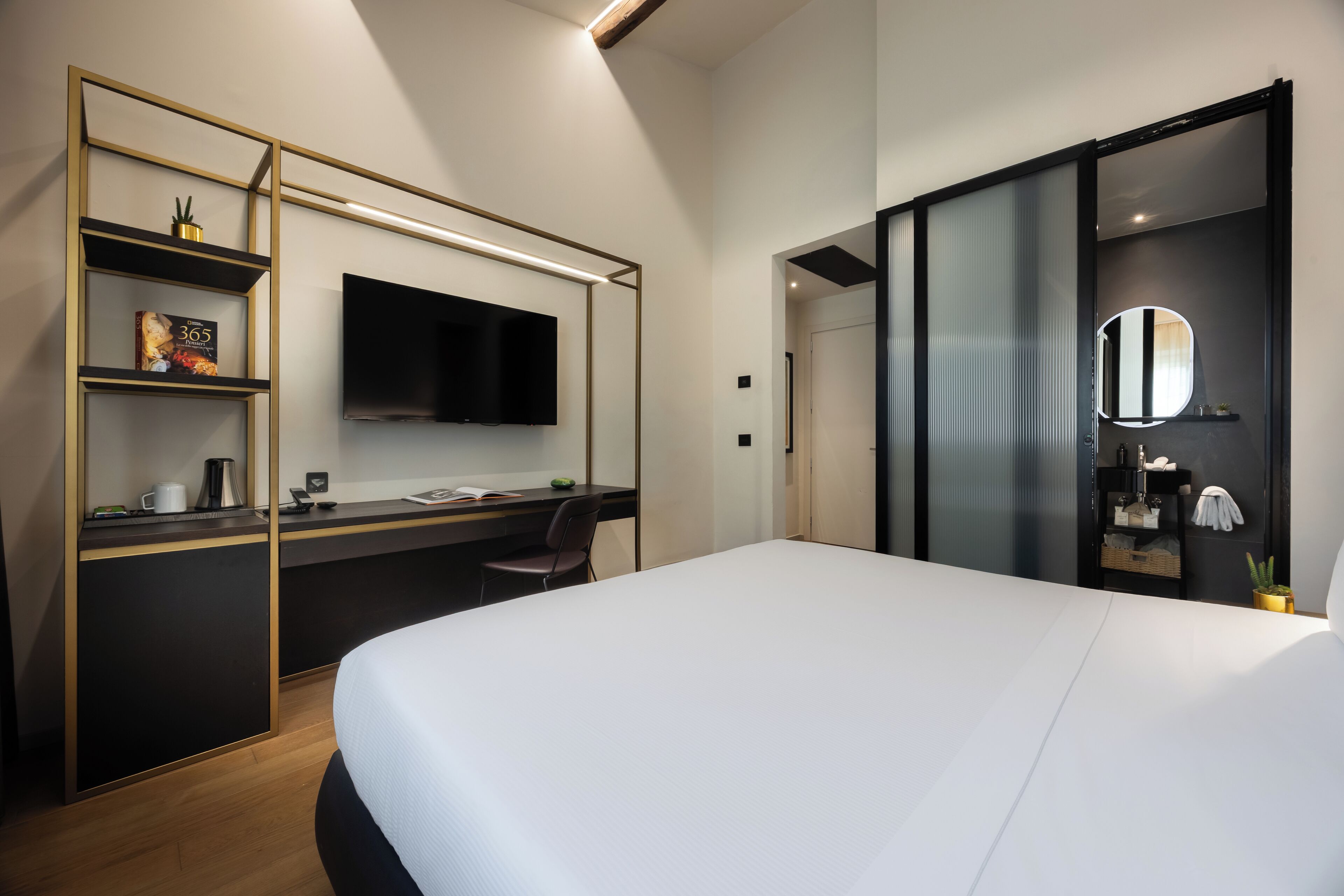 Ein modernes Hotelzimmer mit einem großen Bett, einem Schreibtisch, einem Flachbildfernseher, einem Bücherregal und einem begehbaren Kleiderschrank.